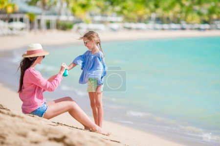 Téléchargez les photos : Jeune mère appliquant de la crème solaire sur sa fille - en image libre de droit