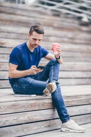 Photo for Man is reading text message on mobile phone while walking in the park - Royalty Free Image