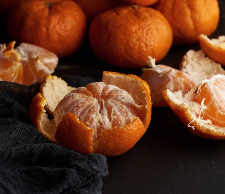 Téléchargez les photos : Mandarines mûres rondes pelées dans une assiette sur une serviette textile noire - en image libre de droit