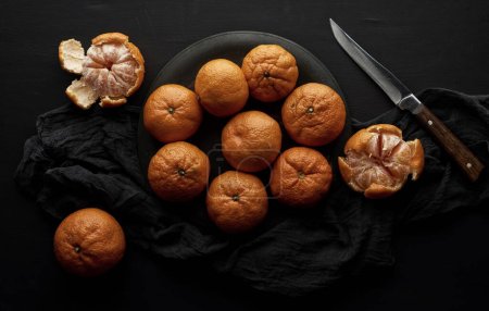 Foto de Mandarinas maduras redondas en un plato sobre una servilleta textil negra - Imagen libre de derechos