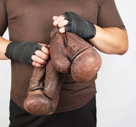 Téléchargez les photos : Homme adulte en uniforme de sport brun tient une paire de gants vintage marron - en image libre de droit