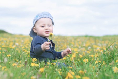 Foto de Un niño pequeño con gorra de béisbol se sienta en un prado. - Imagen libre de derechos
