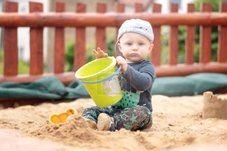 Téléchargez les photos : Un garçon caucasien dans une casquette de baseball est assis dans un bac à sable - en image libre de droit