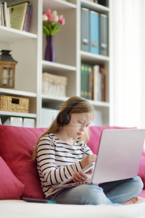 Photo for Young schoolgirl doing her homework with digital tablet at home. Child using gadgets to study. Education and distance learning for kids. Homeschooling during quarantine. - Royalty Free Image