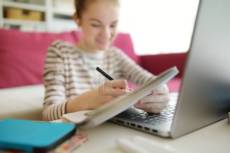 Photo for Preteen schoolgirl doing her homework with laptop computer at home. Child using gadgets to study. Online education and distance learning for kids. Homeschooling during quarantine - Royalty Free Image