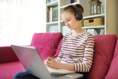 Photo for Preteen schoolgirl doing her homework with laptop computer at home. Child using gadgets to study. Online education and distance learning for kids. Homeschooling during quarantine. - Royalty Free Image