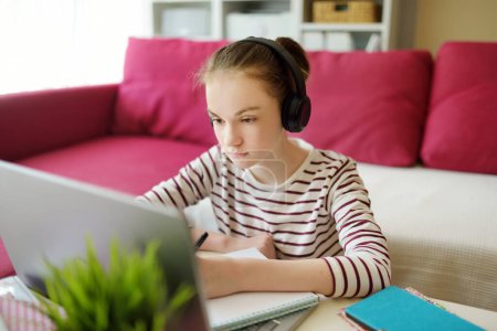 Photo for Preteen schoolgirl doing her homework with laptop computer at home. Child using gadgets to study. Online education and distance learning for kids. Homeschooling during quarantine - Royalty Free Image