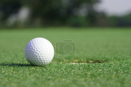Téléchargez les photos : Gros plan sur une balle de golf sur une herbe verte près du trou - en image libre de droit