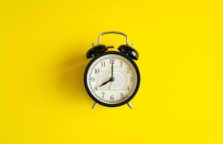 Téléchargez les photos : "black alarm clock from 7 a.m. to 8 a.m. with bright yellow  back" - en image libre de droit