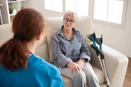 Téléchargez les photos : "Vue arrière de l'infirmière dans une maison de soins infirmiers parlant avec une femme retraitée" - en image libre de droit