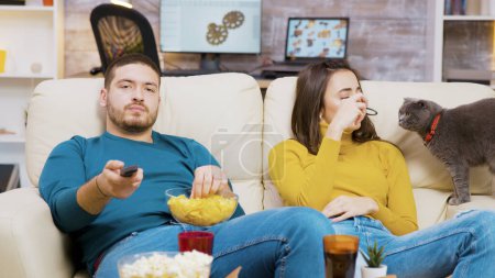 Foto de Hombre barbudo comiendo patatas fritas y usando control remoto para cambiar los canales de televisión - Imagen libre de derechos