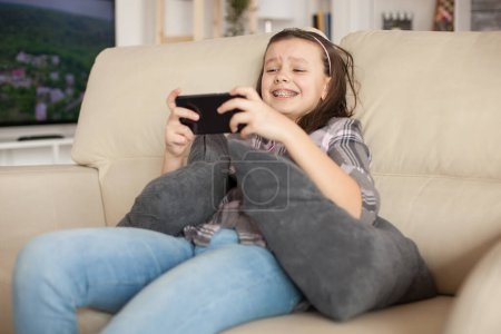 Photo for Cheerful little girl playing video games on smartphone - Royalty Free Image