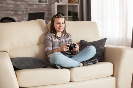 Foto de Niña con aparatos ortopédicos se sienta en el sofá jugando videojuegos - Imagen libre de derechos