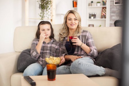 Photo for Mother and daughter watching a movie sitting on the couch - Royalty Free Image