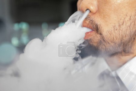 Foto de El hombre con barba fuma y echa humo. - Imagen libre de derechos