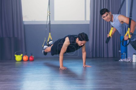 Photo for "Group of sports people are training indoors with TRX. Two attrac" - Royalty Free Image