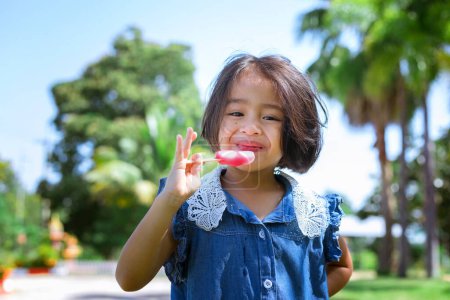 Photo for Cute little girl eating popsicle with sunset background - Royalty Free Image