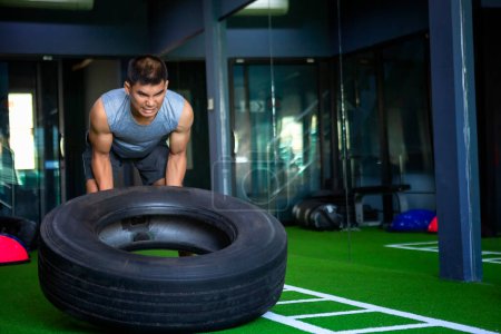 Photo for Strong muscular man lifts tire as part of his fitness program. - Royalty Free Image