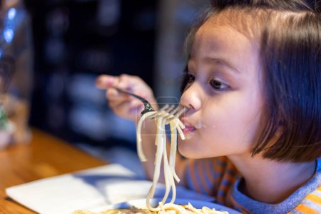 Téléchargez les photos : "Asian little girl is eating spaghetti bolognese in the restauran" - en image libre de droit