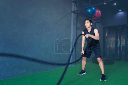 Foto de Hombre usando una camiseta para ejercitarse en el gimnasio con cuerdas de batalla - Imagen libre de derechos