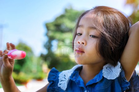 Téléchargez les photos : Mignonne petite fille manger popsicle avec coucher de soleil fond - en image libre de droit