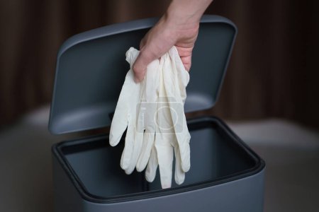 Téléchargez les photos : Mettre à la main des gants chirurgicaux sales usagés dans une poubelle. - en image libre de droit