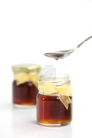 Téléchargez les photos : Miel coulant de la cuillère sur le dessus du bocal, isolé sur fond blanc - en image libre de droit