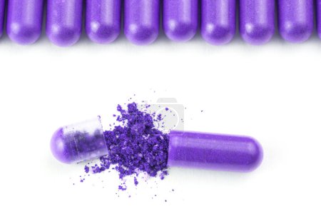 Foto de "fila de cápsulas orgánicas de color púrpura protón aisladas sobre fondo blanco de cerca con una abierta
" - Imagen libre de derechos