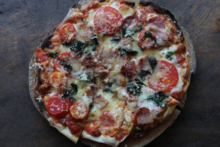 Foto de Pizza tocino jamón tomate y queso en la parte superior sobre fondo de madera - Imagen libre de derechos
