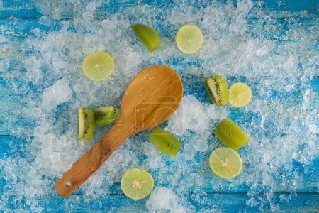 Foto de Cubos de hielo picado y limón, kiwi, cuchara de madera en azul vintage - Imagen libre de derechos