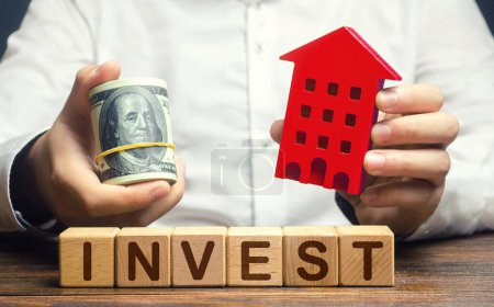 Photo for Man with dollars and house figurine and word Invest. Real estate financial investment. Favorable investment climate, cheap housing and low demand. Saving savings in a crisis. Rental business - Royalty Free Image