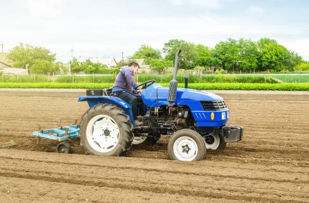 Photo for Caucasian farmer on a tractor making rows on a farm field. Preparing the land for planting future crop plants. Cultivation of soil for planting. Agroindustry, agribusiness. Farming, farmland - Royalty Free Image
