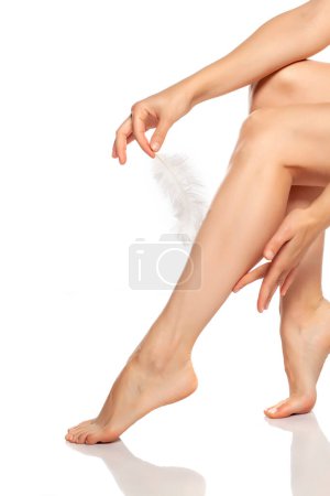Téléchargez les photos : Femme touchant ses belles jambes avec plume sur fond blanc - en image libre de droit
