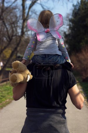 Téléchargez les photos : Père portant une petite fille tout-petit, avec des ailes de papillon - en image libre de droit