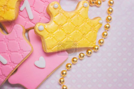 Téléchargez les photos : "Premier anniversaire, biscuits royaux glacés en forme de couronne sur fond rose" - en image libre de droit