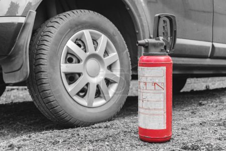 Téléchargez les photos : Un extincteur se tient sur le sol près de la voiture comme sécurité incendie. Prévention des incendies routiers - en image libre de droit