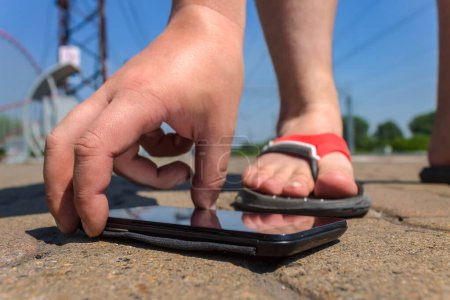 Foto de Un hombre levanta un teléfono inteligente en un parque público caído en la carretera - Imagen libre de derechos