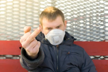 Photo for An impolite man in a medical mask shows an obscene and bad gesture with the middle finger - Royalty Free Image