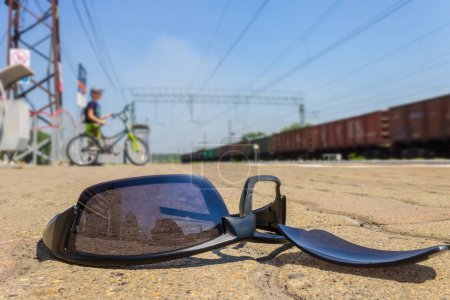 Photo for The broken glasses lie at the railway station against the background of passing by the boy by bicycle and moving train - Royalty Free Image