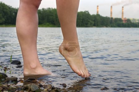 Foto de Feet girl in the river on the background of the factory pipes releasing smoke - Imagen libre de derechos