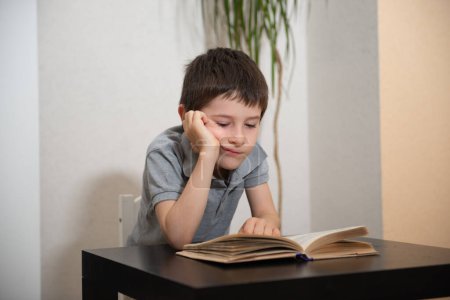 Photo for A schoolboy a bored face reads a book - Royalty Free Image