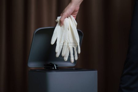 Téléchargez les photos : Mettre à la main des gants chirurgicaux sales usagés dans une poubelle. - en image libre de droit