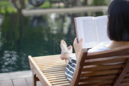 Téléchargez les photos : Femme lecture et détente près de la piscine de luxe - en image libre de droit