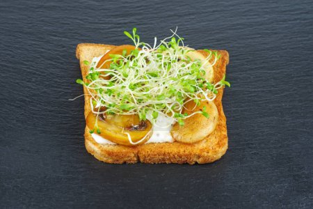 Foto de Brotes de alfalfa verde, champiñones a la parrilla en rebanadas tostadas de pan integral sobre fondo de pizarra de piedra negra - Imagen libre de derechos