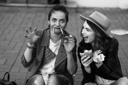 Téléchargez les photos : Filles drôles manger hamburger et pommes de terre frites dans la rue - en image libre de droit
