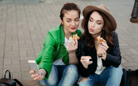 Foto de Chicas positivas comiendo hamburguesas y tomando autorretrato - Imagen libre de derechos