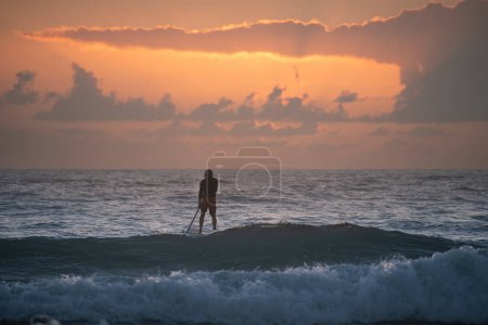 Téléchargez les photos : Silhouette de femme sur paddle board à la plage au coucher du soleil - en image libre de droit