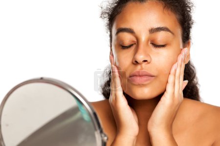 Photo for Portrait of a young dark-skinned woman applying cream on her face - Royalty Free Image