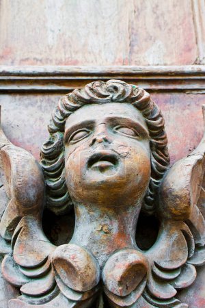 Foto de Escultura de un viejo ángel de madera contra una puerta de madera de una iglesia - Imagen libre de derechos