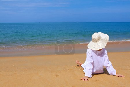 pintoresca foto de mujer joven con ropa blanca y sombrero pasar tiempo en la playa durante las vacaciones